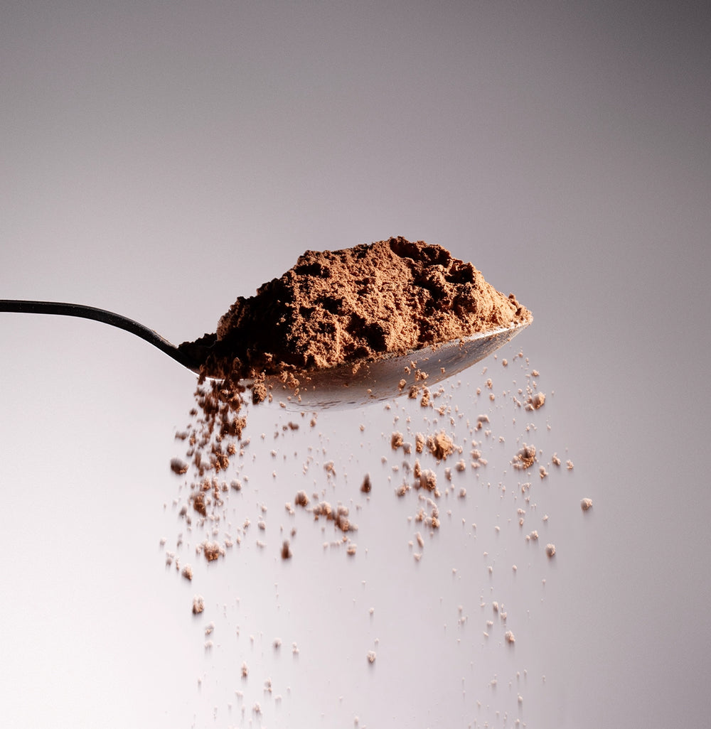 Dolce Superfoods organic cacao powder on metal spoon with falling powder