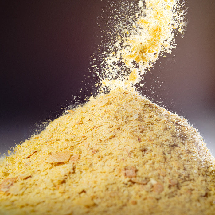 Golden nutritional yeast flakes falling into a pile against a moody dark background — Dolce Superfoods bulk nutritional yeast