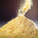 Golden nutritional yeast flakes falling into a pile against a moody dark background — Dolce Superfoods bulk nutritional yeast