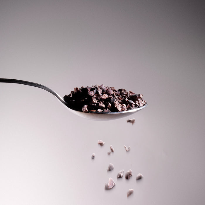 Dolce Superfoods organic cacao nibs on metal spoon with falling pieces