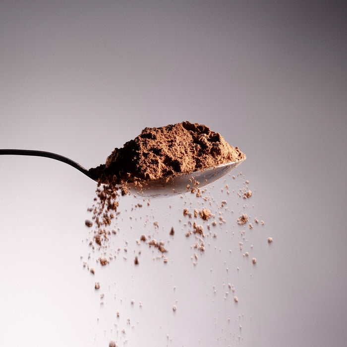 Dolce Superfoods organic cacao powder on metal spoon with falling powder