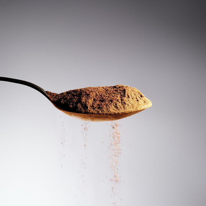 Dolce Superfoods organic instant coffee powder on spoon against light background