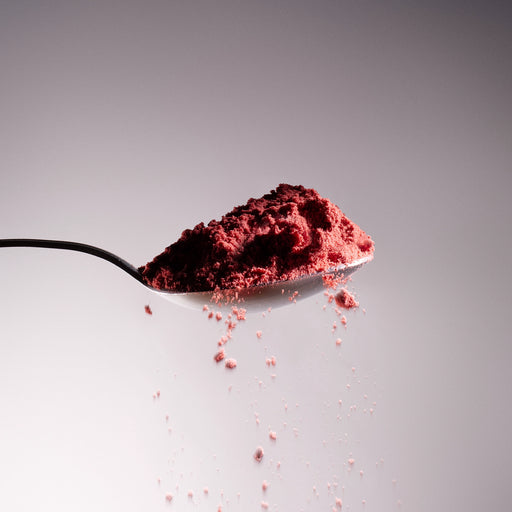 Dolce Superfoods organic strawberry powder on spoon against light background