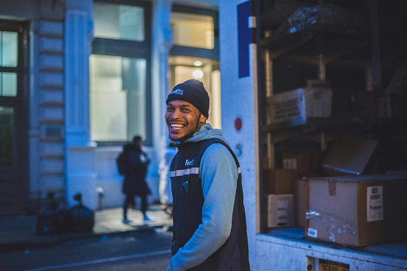 Man in a FedEx vest standing next to a delivery truck at night.